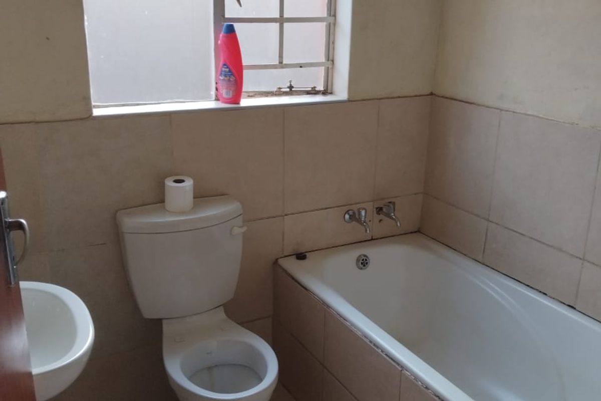 A functional bathroom featuring a standard bathtub, toilet, and wall-mounted basin with neutral wall and floor tiling.