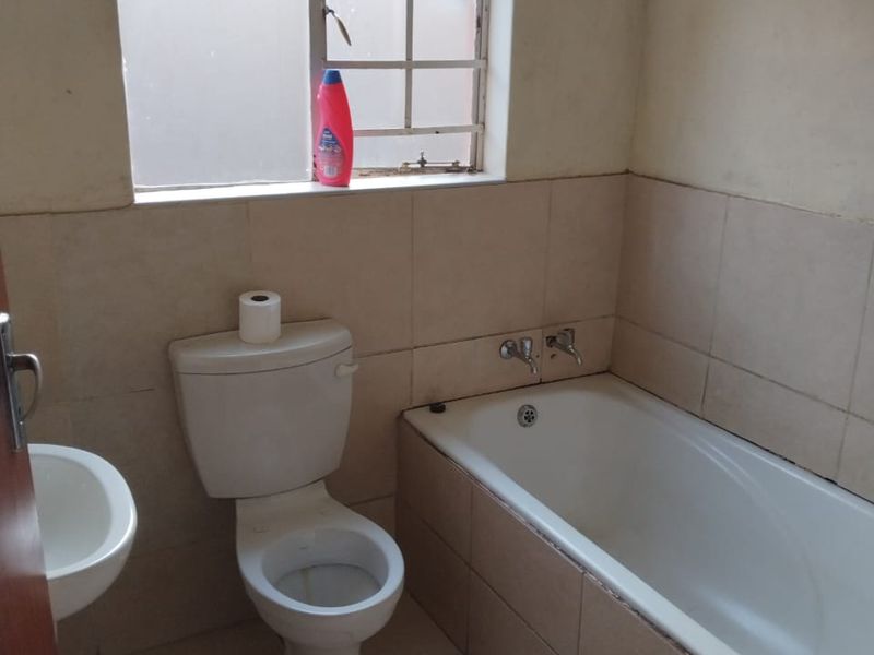 A functional bathroom featuring a standard bathtub, toilet, and wall-mounted basin with neutral wall and floor tiling.