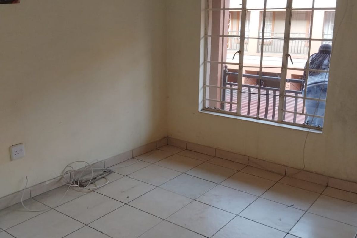 An empty bedroom featuring tiled flooring, security bars on the window, and a curtain rail, ready for personalization.