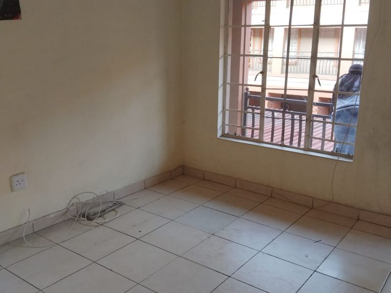 An empty bedroom featuring tiled flooring, security bars on the window, and a curtain rail, ready for personalization.