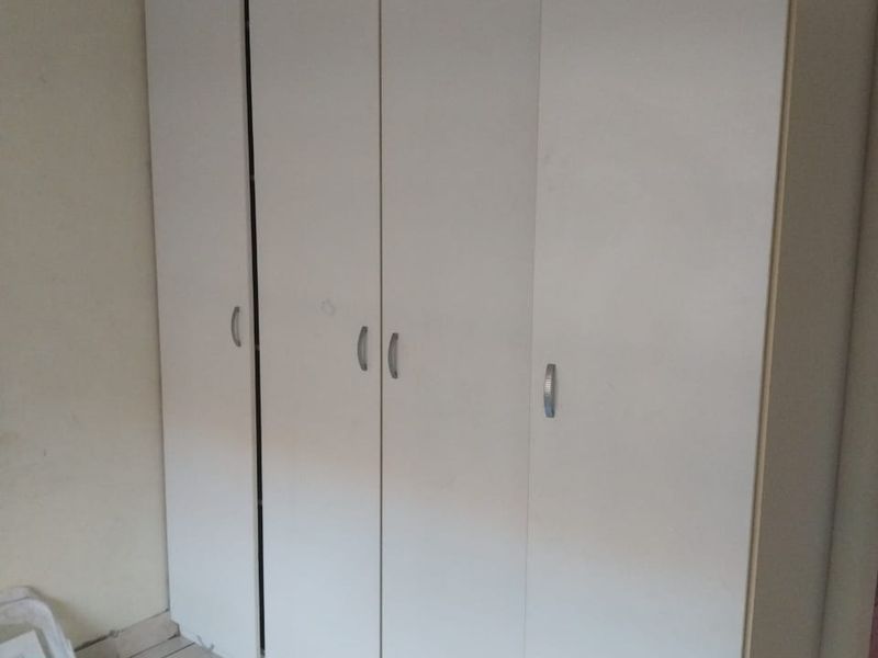 A bedroom featuring white built-in cupboards and tiled flooring, offering ample storage space.