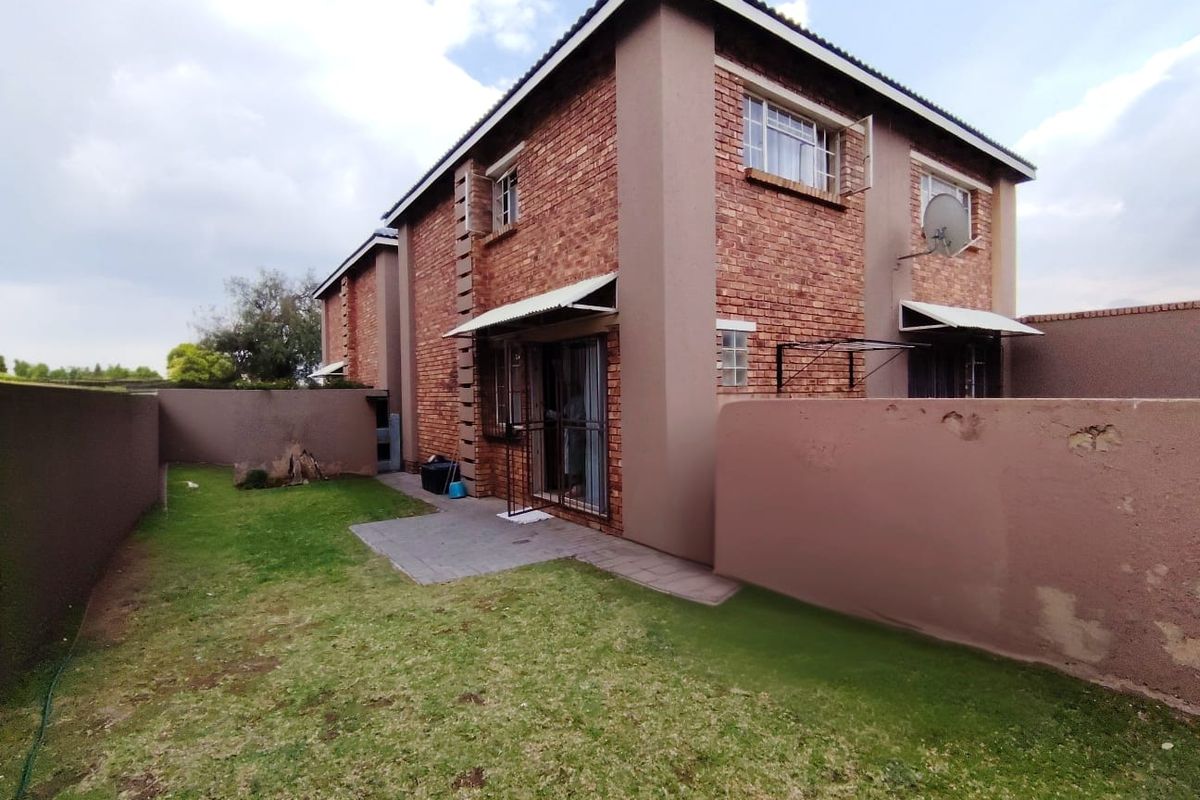 Rear view of the townhouse featuring a brick facade, paved patio area, and a private garden enclosed by a boundary wall.