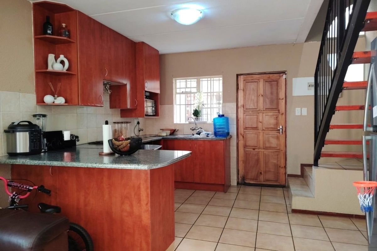 Kitchen featuring laminate cabinetry, granite countertops, and tiled flooring, with an adjacent staircase leading to the upper level.