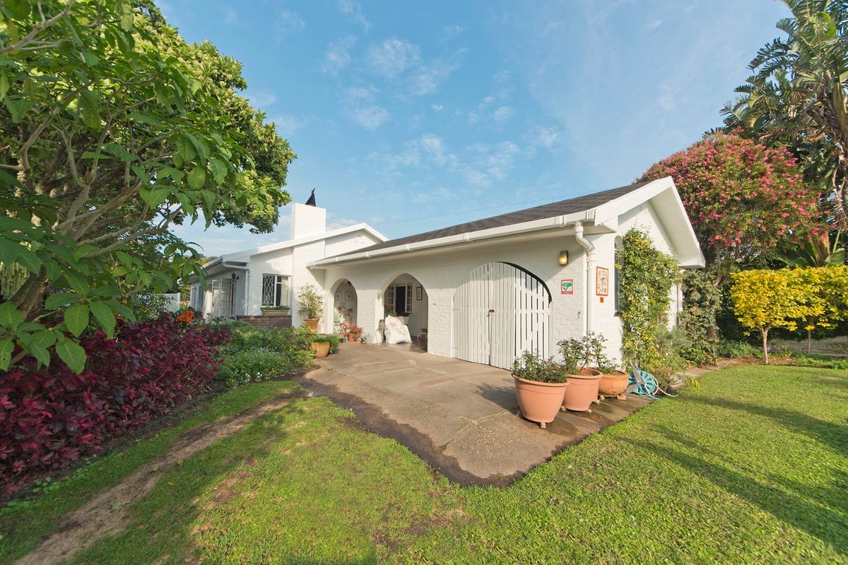 A charming white-painted exterior rear view featuring a covered patio with arched architectural details, a brick chimney, and a well-maintained garden setting.