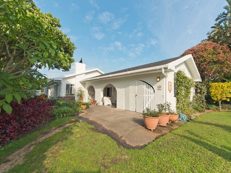 A charming white-painted exterior rear view featuring a covered patio with arched architectural details, a brick chimney, and a well-maintained garden setting.