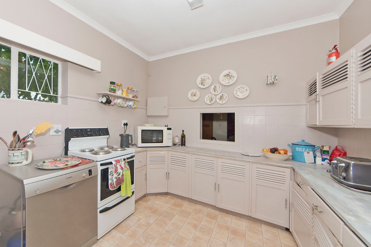A functional kitchen featuring louvered cabinetry, tiled splashbacks, ceramic flooring, and a convenient pass-through window connecting to adjacent living spaces.