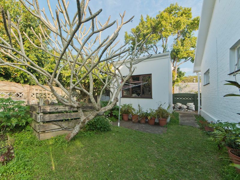 A rear garden area featuring a concrete pathway, established trees, a timber compost bin, and a fixed clothesline alongside the main house structure.