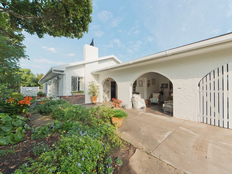 A charming rear exterior view featuring a white painted brick facade, a covered arched patio area, and a well-maintained garden.