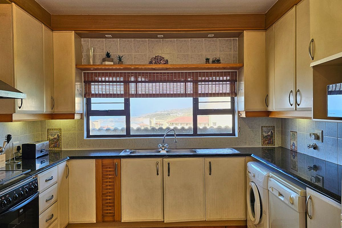 A functional kitchen featuring built-in cabinetry, dark countertops, a stainless steel sink, and integrated laundry plumbing, with a window offering a coastal view.