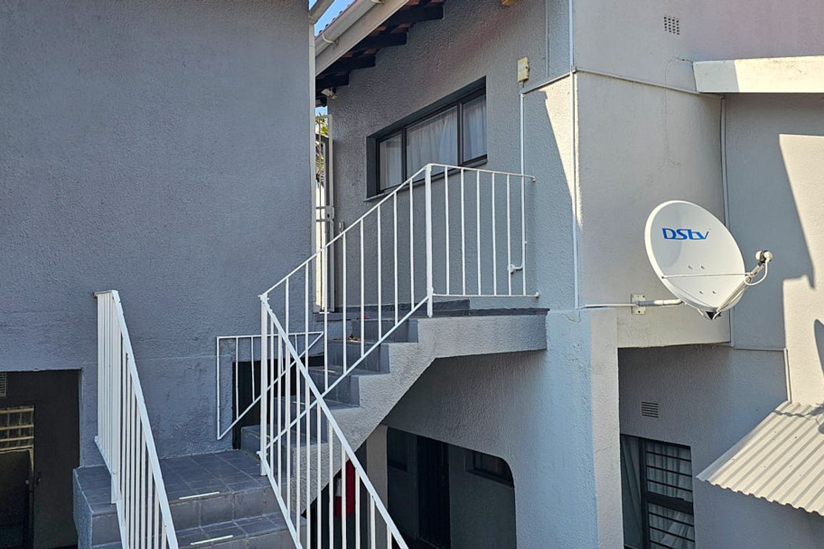 Exterior view of the apartment building featuring a concrete staircase with metal balustrades and a mounted satellite dish.