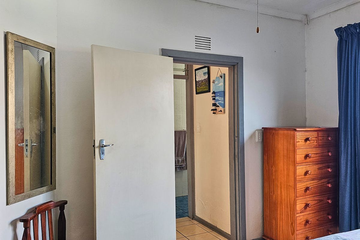 A bedroom featuring a doorway leading to an adjacent tiled bathroom, with visible wear on the door frame and basic interior finishes.