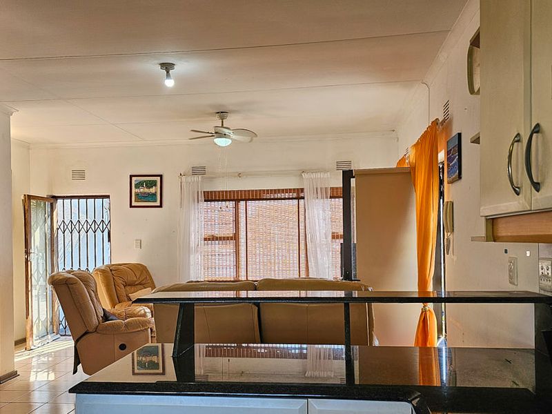Open plan living area featuring a kitchen with granite countertops and cabinetry, flowing into a lounge space with access to a security gate.