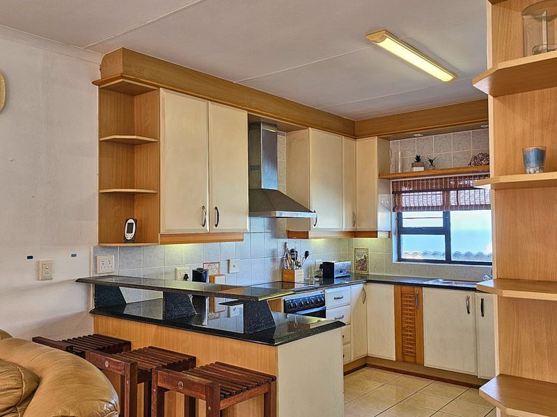 Open plan kitchen featuring light wood cabinetry, granite breakfast bar, tiled backsplash, and built-in shelving, offering a functional and well-lit cooking and dining space.