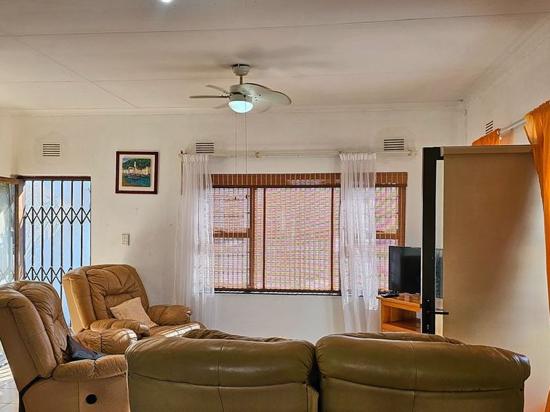 A living room featuring a ceiling fan, security gate, and window treatments, offering a functional space with natural light.