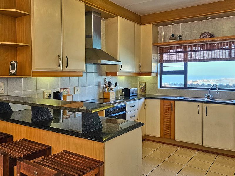 A functional kitchen featuring granite countertops, a breakfast bar, built-in cabinetry, and a stainless steel extractor fan, with a window offering a scenic view.