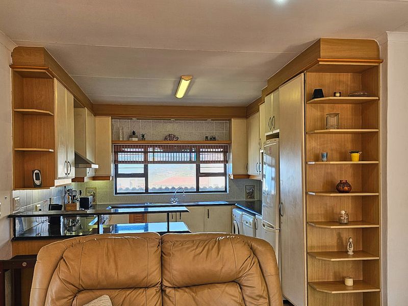 A functional kitchen featuring built-in wooden cabinetry, laminate countertops, a tiled backsplash, and integrated shelving, offering a practical layout with a view.