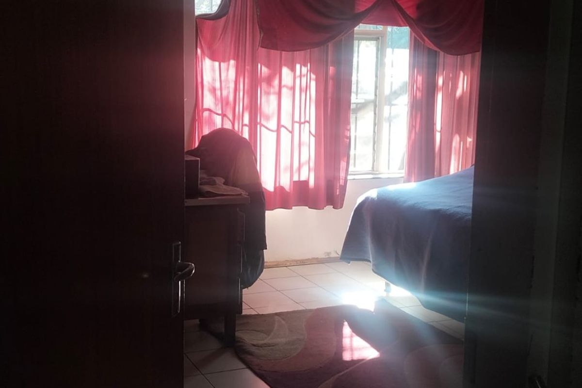 A bedroom featuring tiled flooring and natural light entering through a window, viewed from the doorway.