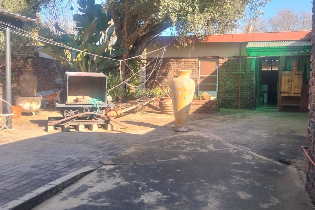A rear courtyard area featuring brick construction, paved sections, and a concrete driveway leading to the main dwelling entrance.