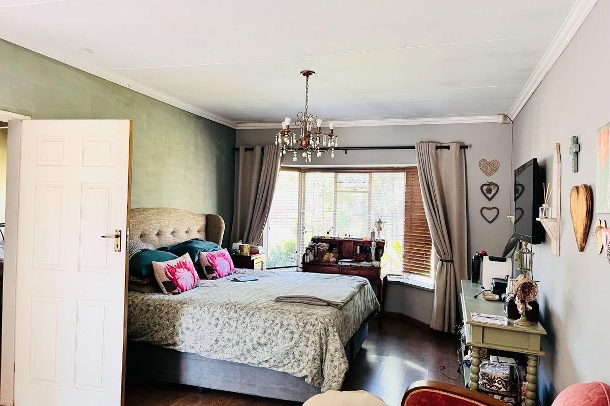 A well-lit bedroom featuring laminate flooring, a classic bay window, and decorative ceiling cornicing, creating a comfortable and inviting living space.