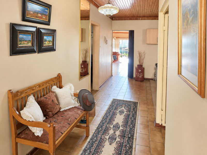 A well-lit hallway featuring warm timber tongue and groove ceiling paneling, ceramic floor tiles, and a full-length wall mirror leading toward the living area.
