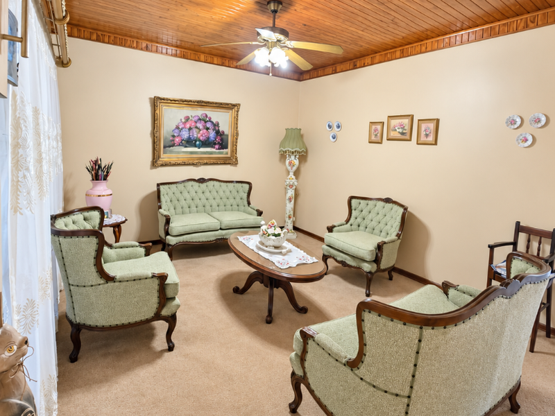 A formal living room featuring a warm timber tongue and groove ceiling, ceiling fan, and neutral carpet flooring.