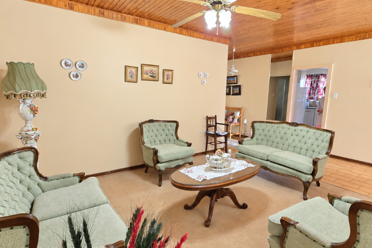 A traditional living room featuring a warm timber tongue and groove ceiling, ceiling fan, and neutral carpeting, offering a classic and comfortable living space.