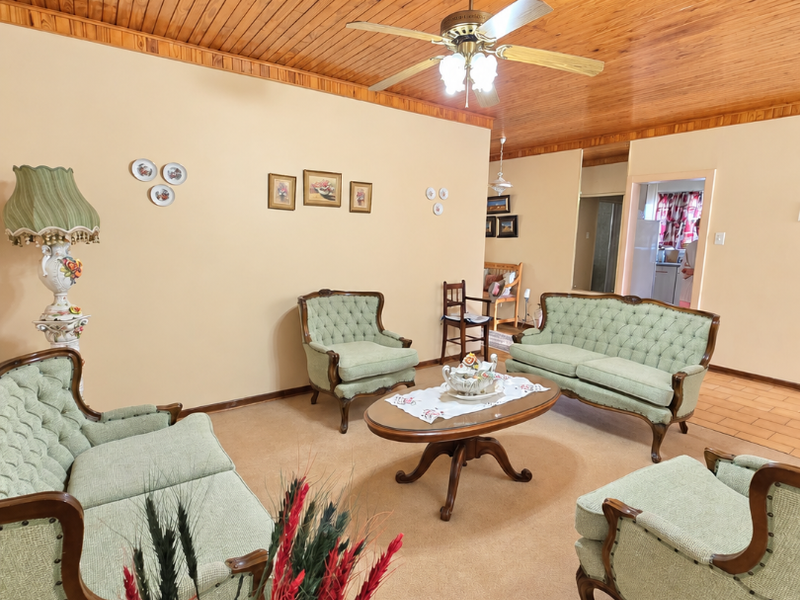 A traditional living room featuring a warm timber tongue and groove ceiling, ceiling fan, and neutral carpeting, offering a classic and comfortable living space.