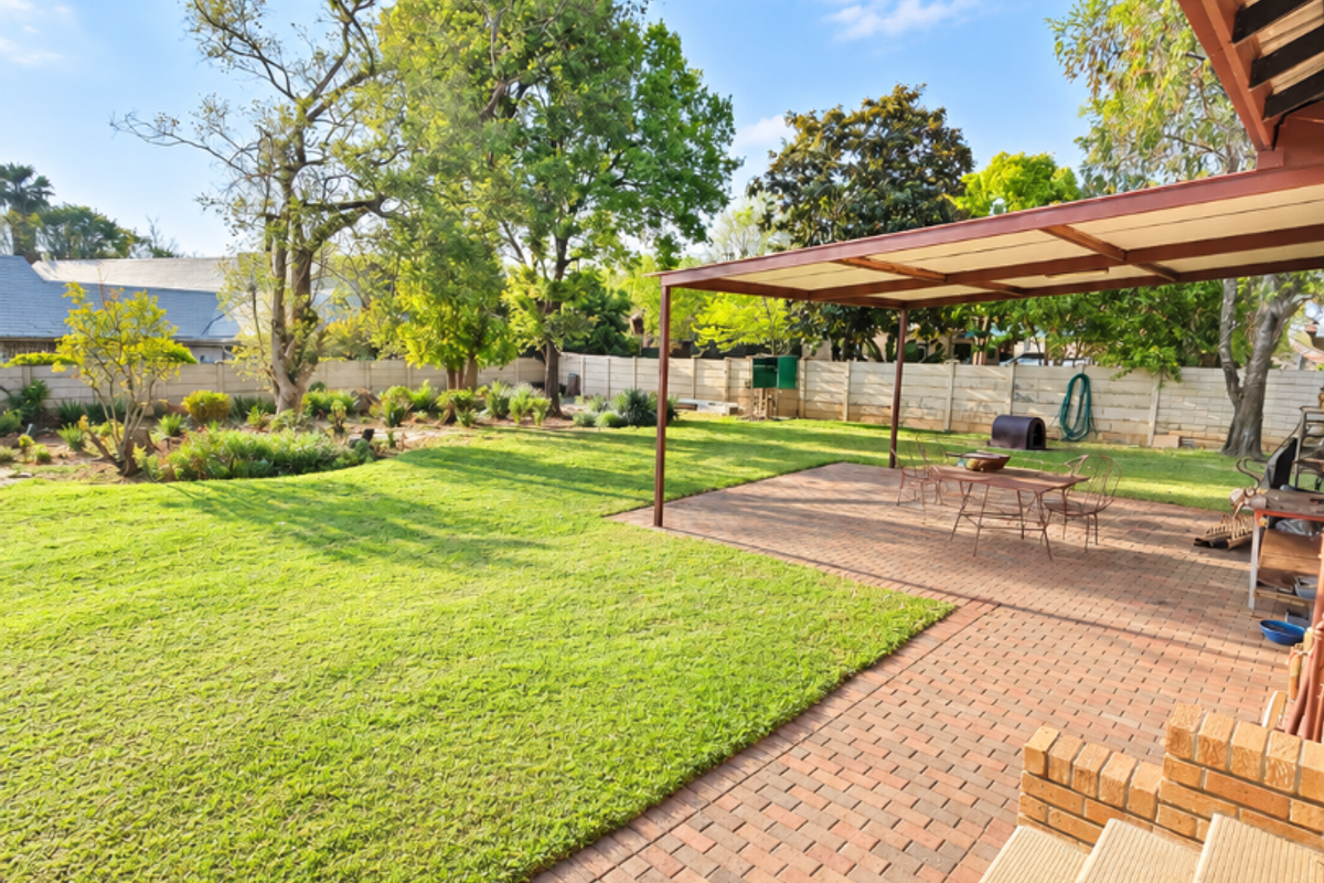 Spacious rear garden featuring a paved patio area with a covered pergola, well-maintained lawn, and secure brick boundary walls.