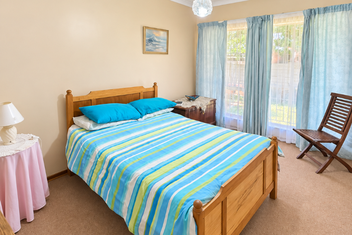 A well-lit bedroom featuring neutral wall tones, carpeted flooring, and large windows with curtain treatments, providing a comfortable and functional living space.