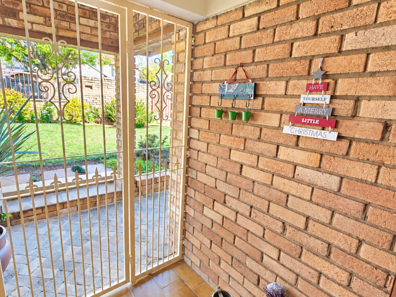 A covered entrance area featuring exposed brick walls, tiled flooring, and a secure metal gate leading to the garden.