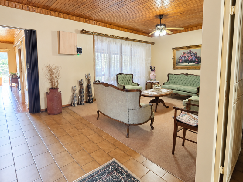 Spacious living room featuring a warm timber tongue and groove ceiling, ceiling fan, and a combination of tiled and carpeted flooring.