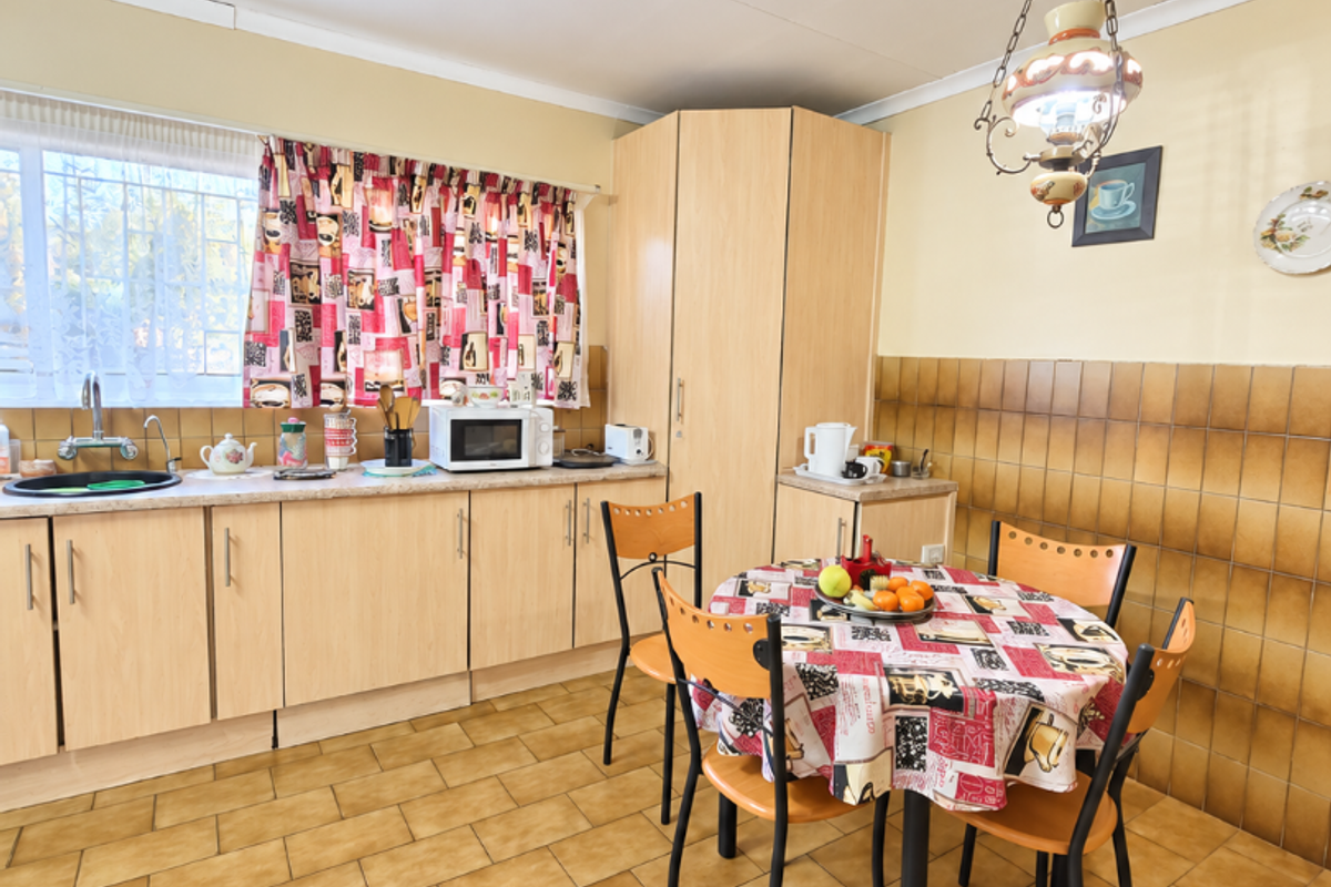 A dated kitchen featuring laminate cabinetry, ceramic tile backsplash, and tiled flooring, offering a functional layout with a dedicated dining area.