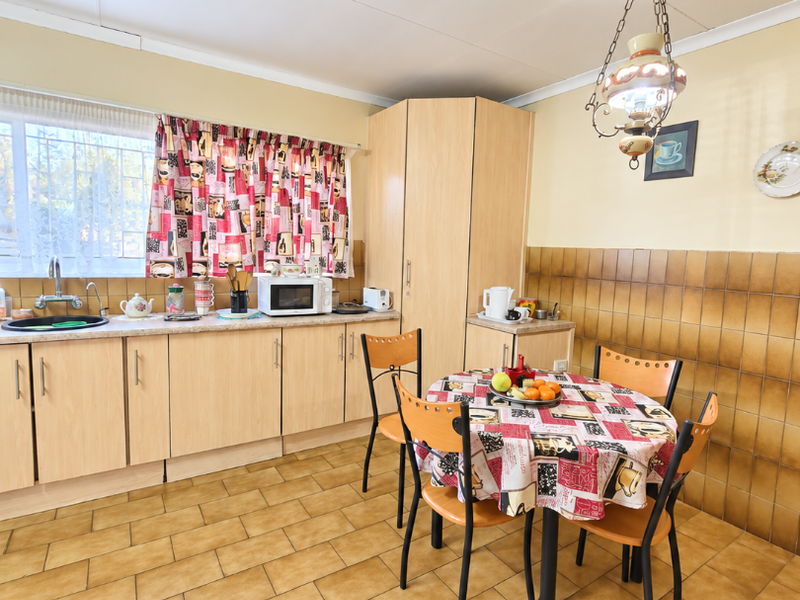 A dated kitchen featuring laminate cabinetry, ceramic tile backsplash, and tiled flooring, offering a functional layout with a dedicated dining area.