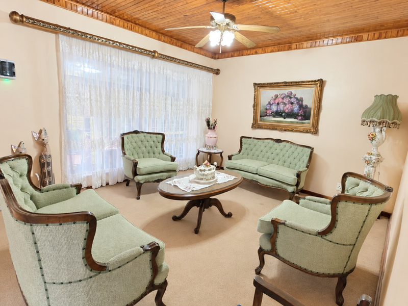 A traditional living room featuring a warm timber tongue and groove ceiling, ceiling fan, and neutral carpeting, offering a classic and comfortable atmosphere.