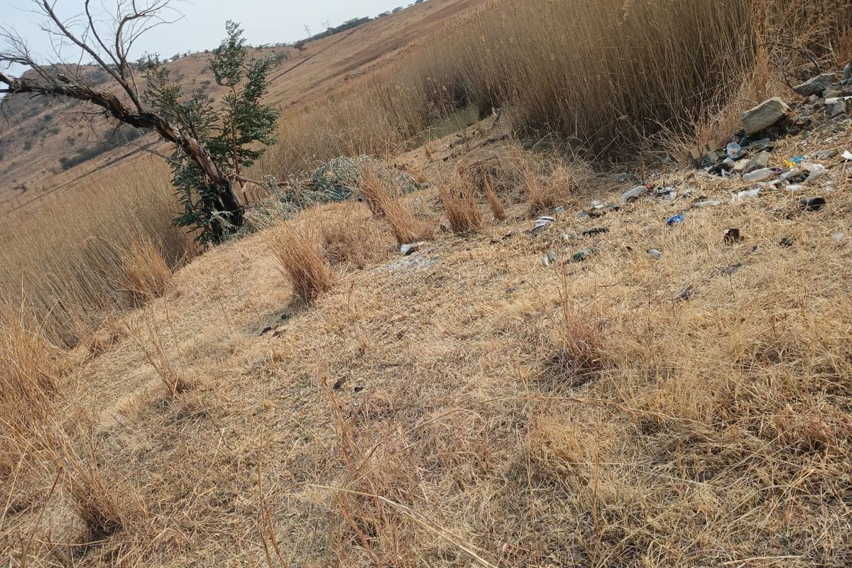 A view of the vacant residential land featuring dry grass, natural vegetation, and visible surface debris.