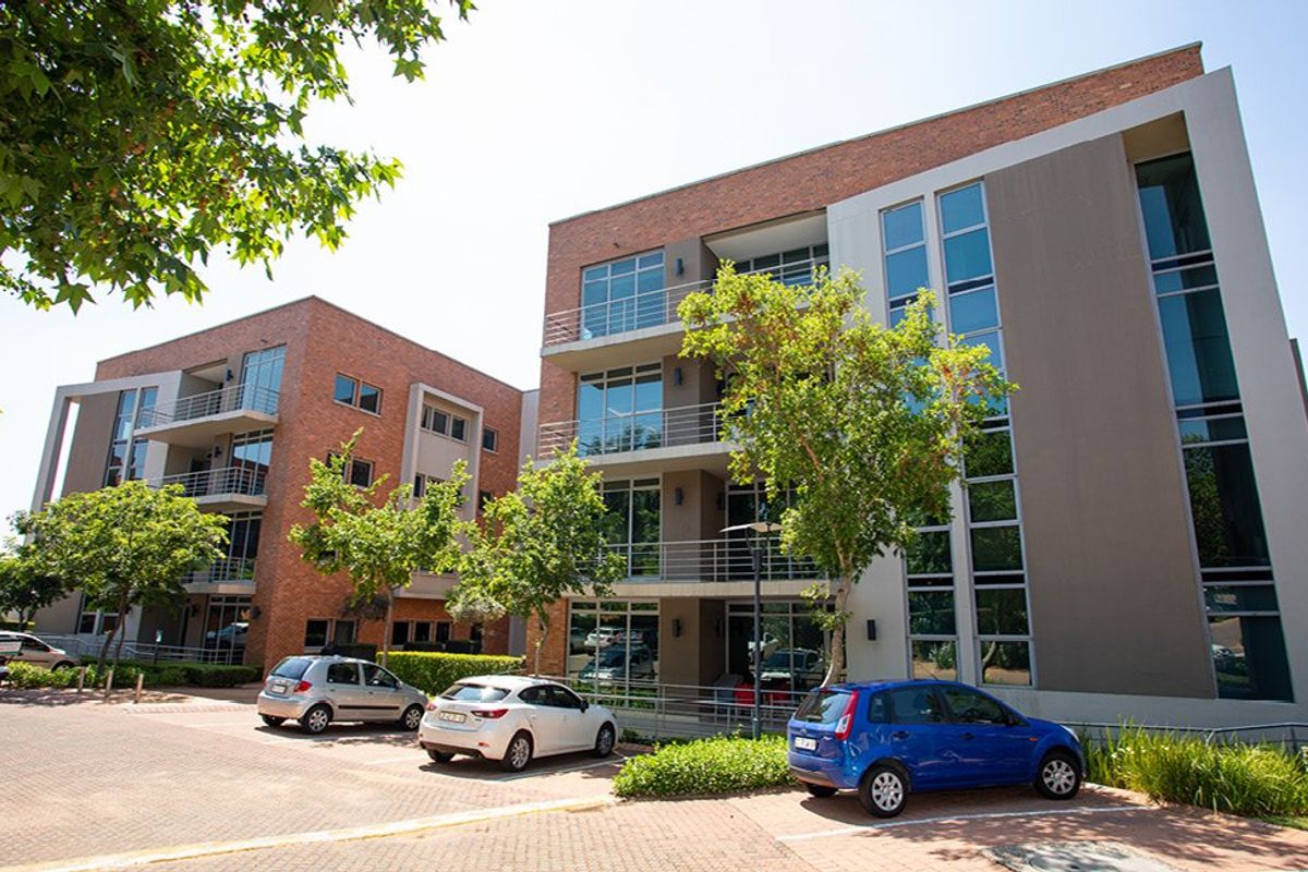 Modern multi-story commercial building featuring a combination of brick and glass facade, private balconies, and an adjacent paved parking area.