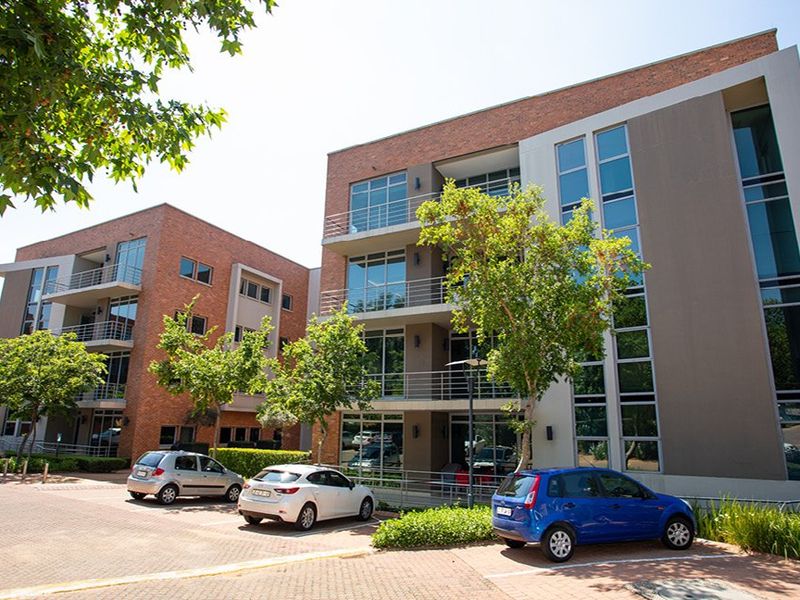 Modern multi-story commercial building featuring a combination of brick and glass facade, private balconies, and an adjacent paved parking area.