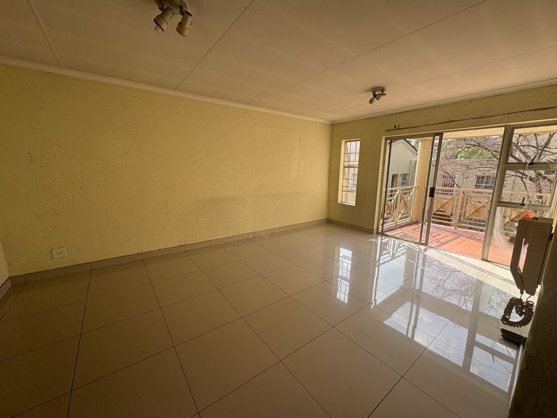 An empty living room featuring tiled flooring, textured walls, and a sliding glass door providing access to a balcony.
