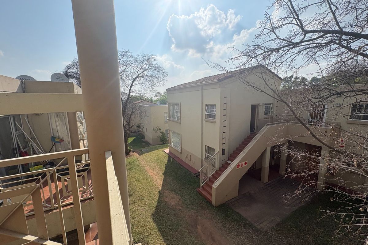 View of the apartment complex exterior featuring a balcony, external staircase, and paved common areas with established landscaping.