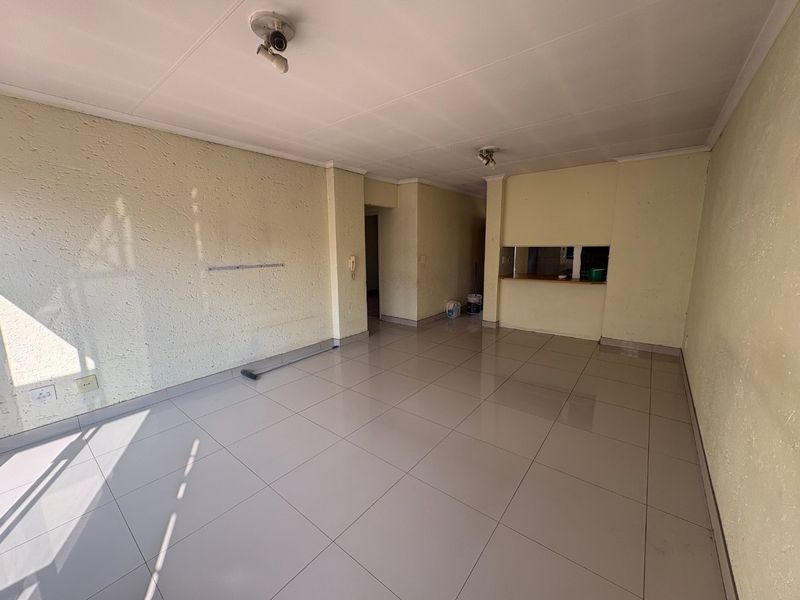 An empty open-plan living area featuring tiled flooring, a pass-through window to the kitchen, and an intercom system.