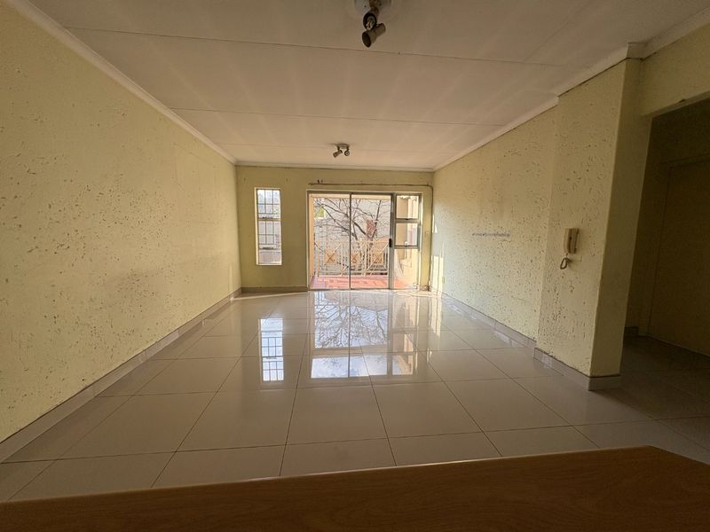 An empty, open-plan living area featuring tiled flooring, textured walls, and a sliding glass door leading to an outdoor balcony.