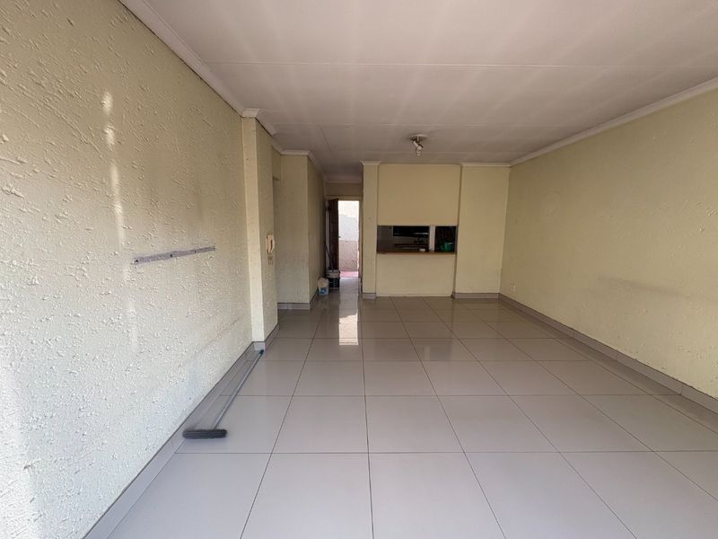 An empty open-plan living area featuring light-colored floor tiles, textured walls, and a convenient pass-through window connecting to the kitchen space.