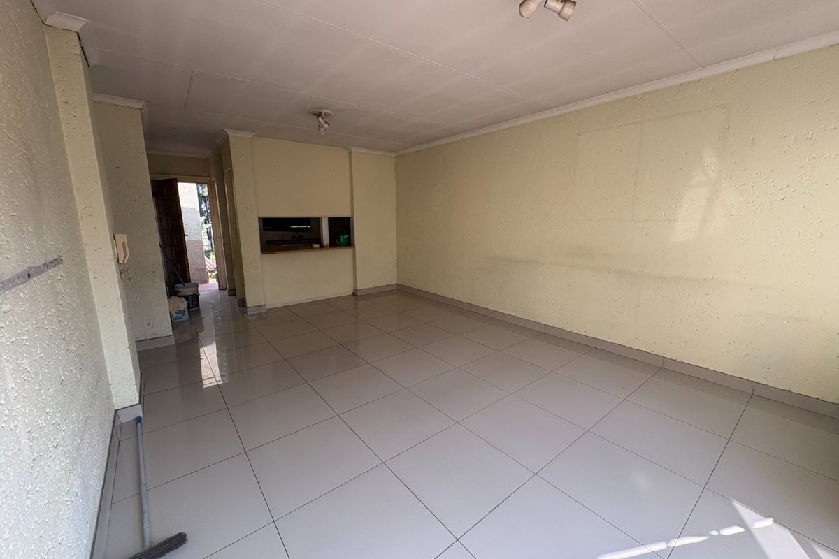 An empty, open-plan living area featuring neutral tiled flooring, textured walls, and a convenient serving hatch connecting to the kitchen space.