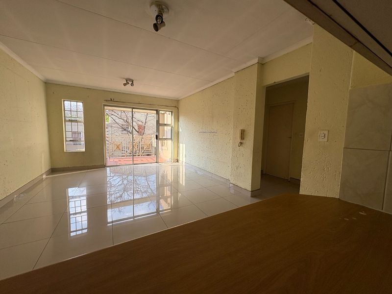 An empty open-plan living area featuring tiled flooring, textured walls, and a sliding glass door leading to a balcony.