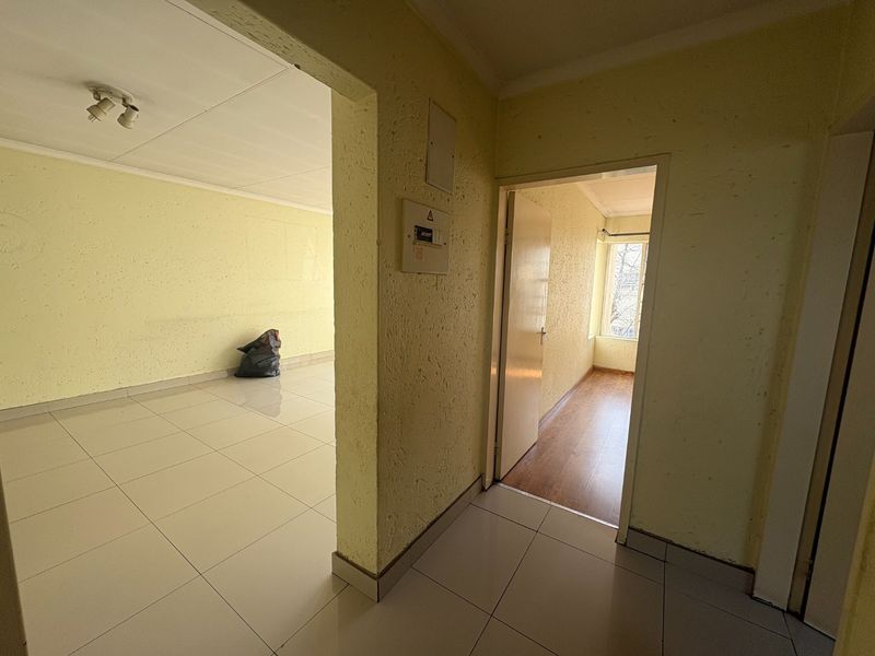 A vacant hallway featuring tiled and laminate flooring, textured walls, and a central electrical distribution board, providing access to adjacent living spaces.