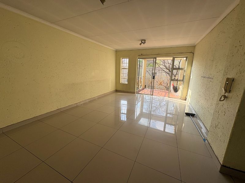 An empty living room featuring tiled flooring, textured walls, and a sliding glass door providing access to an outdoor balcony area.