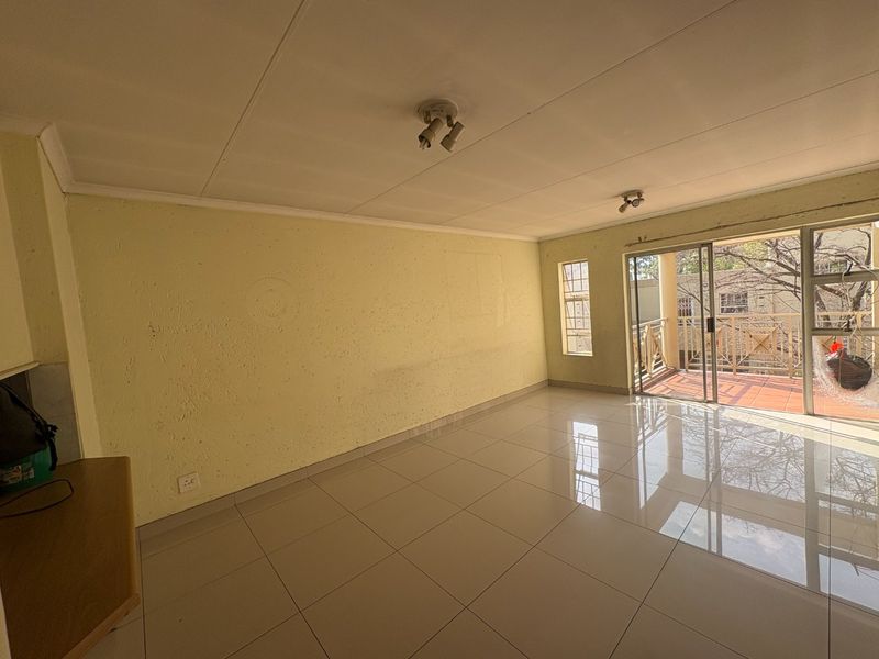 An empty living room featuring tiled flooring, ceiling spotlights, and a sliding glass door providing access to an outdoor balcony area.
