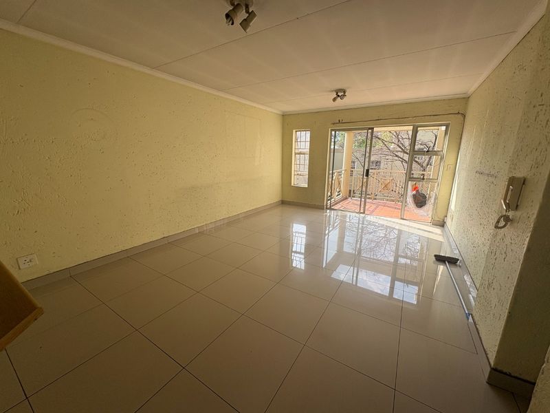 An empty living room featuring tiled flooring, textured walls, and a sliding glass door providing access to a balcony.