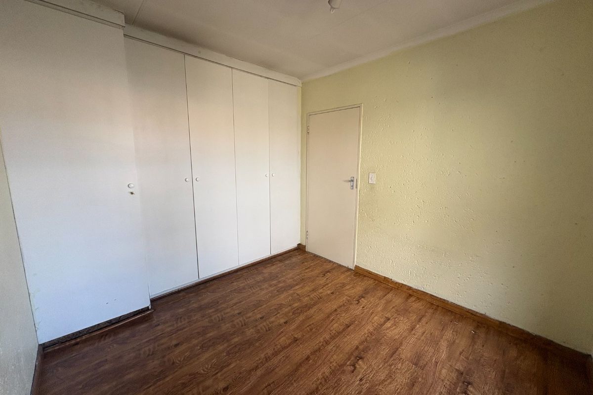 An empty bedroom featuring laminate flooring, built-in cupboards, and a neutral wall finish, offering a blank canvas for personalization.