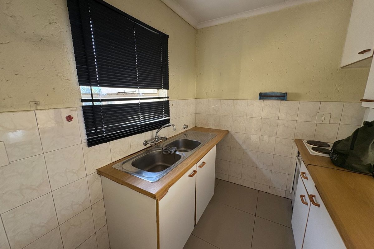 A compact kitchen featuring laminate countertops, a double bowl stainless steel sink, tiled splashbacks, and built-in cabinetry with an integrated electric hob.